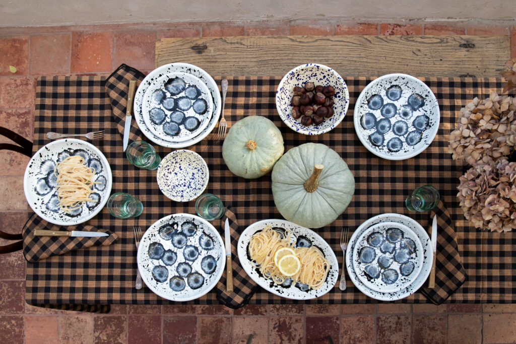 Table avec nappe à carreaux marron, courges bleues de Hongrie en centre de table et vaisselle graphique en acier émaillé.