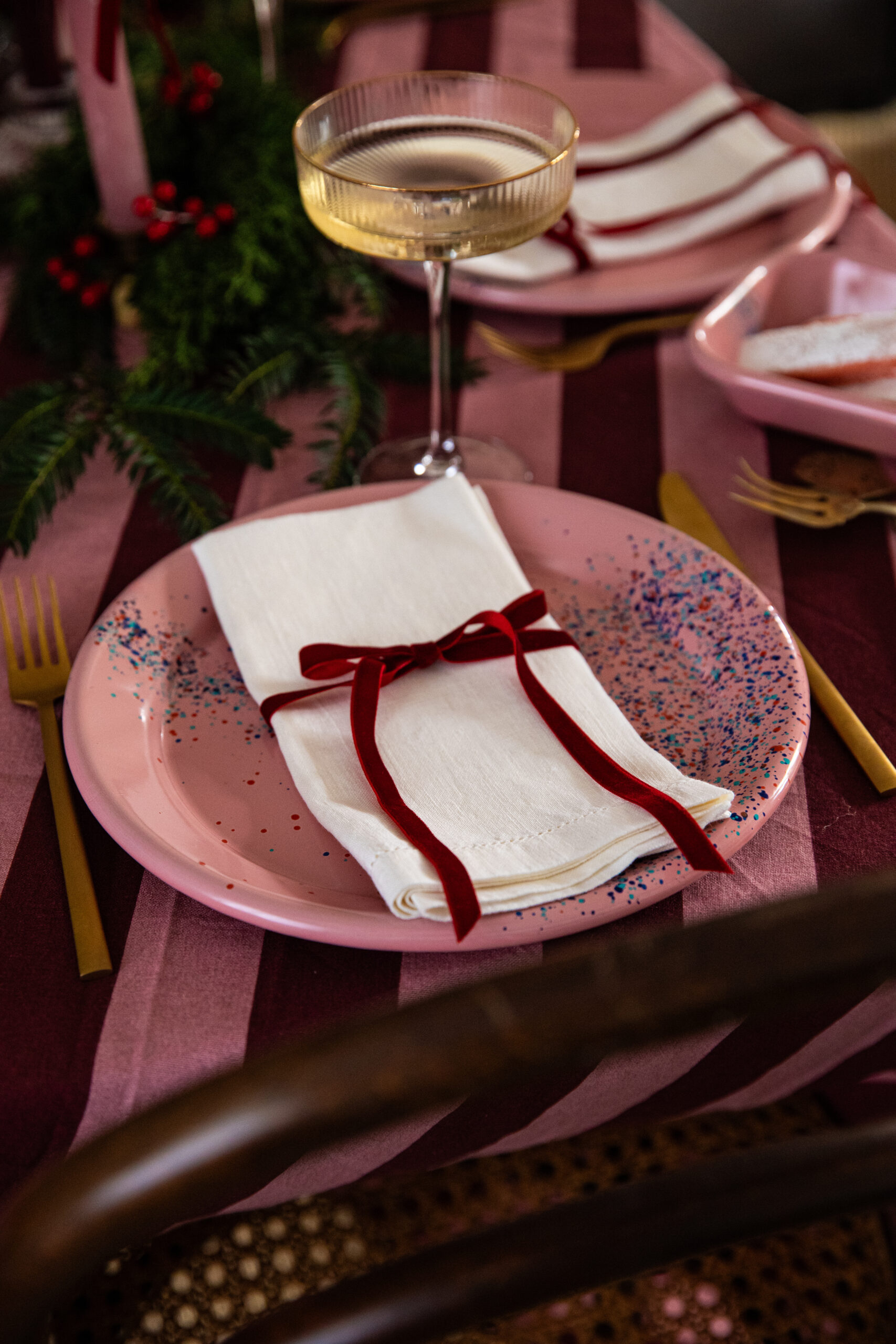 Table de fête rose et bordeaux avec assiette émaillée rose, serviette blanche et nœud en velours bordeaux